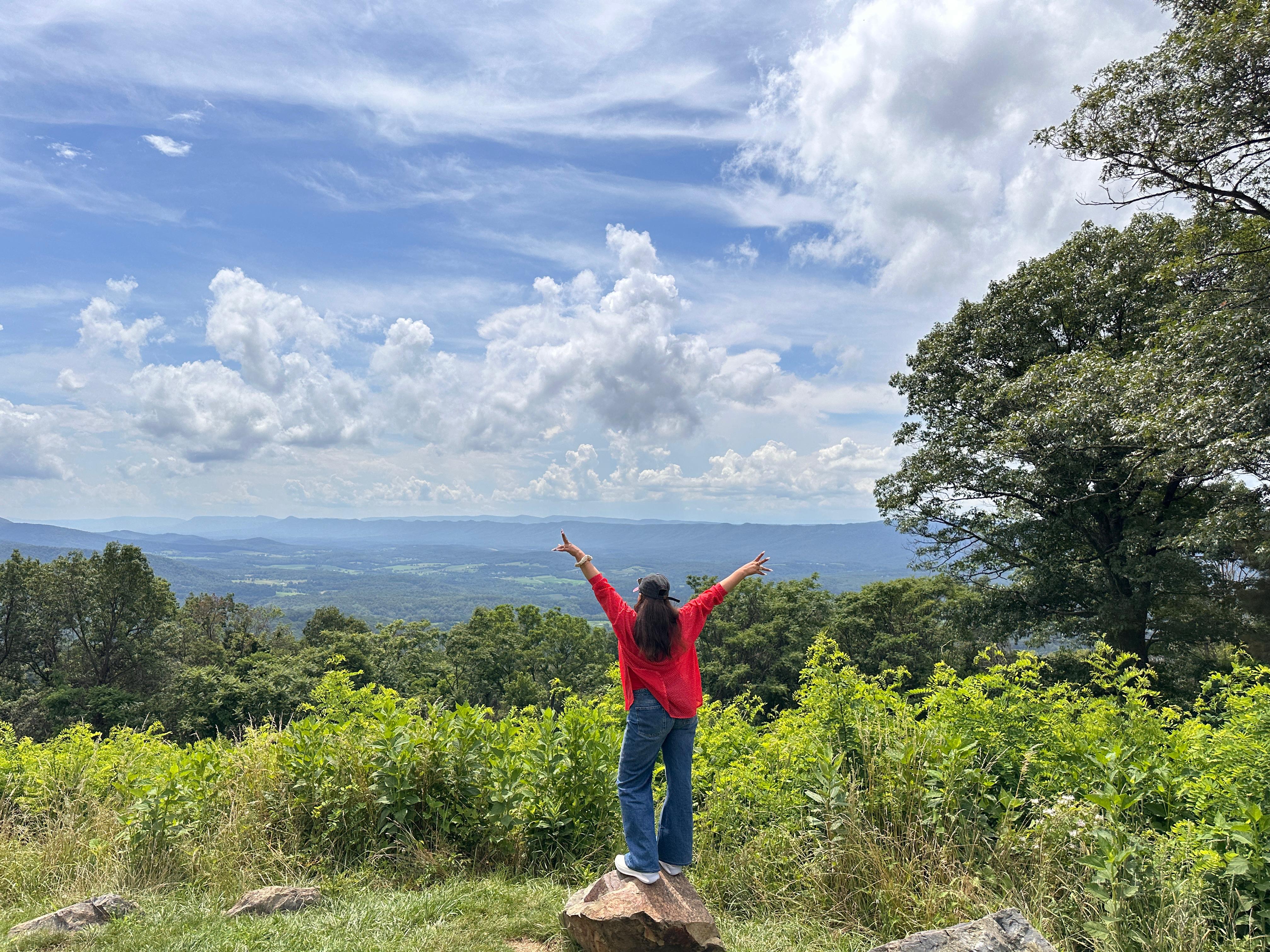 Meena Momand on a mountain overlook, arms raised toward the valley